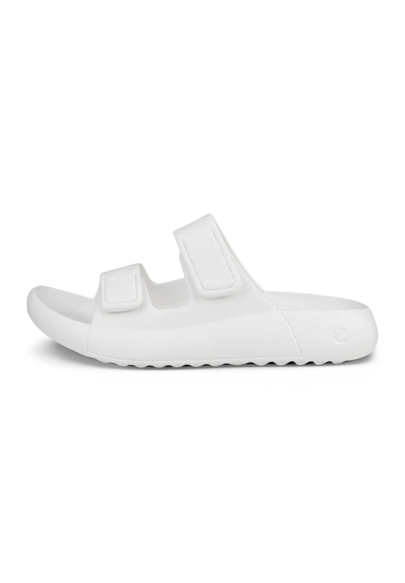 Hvite slip-on sandaler laget av glatt, fleksibelt materiale, med to justerbare borrelåsremmer og en teksturert såle for godt grep.