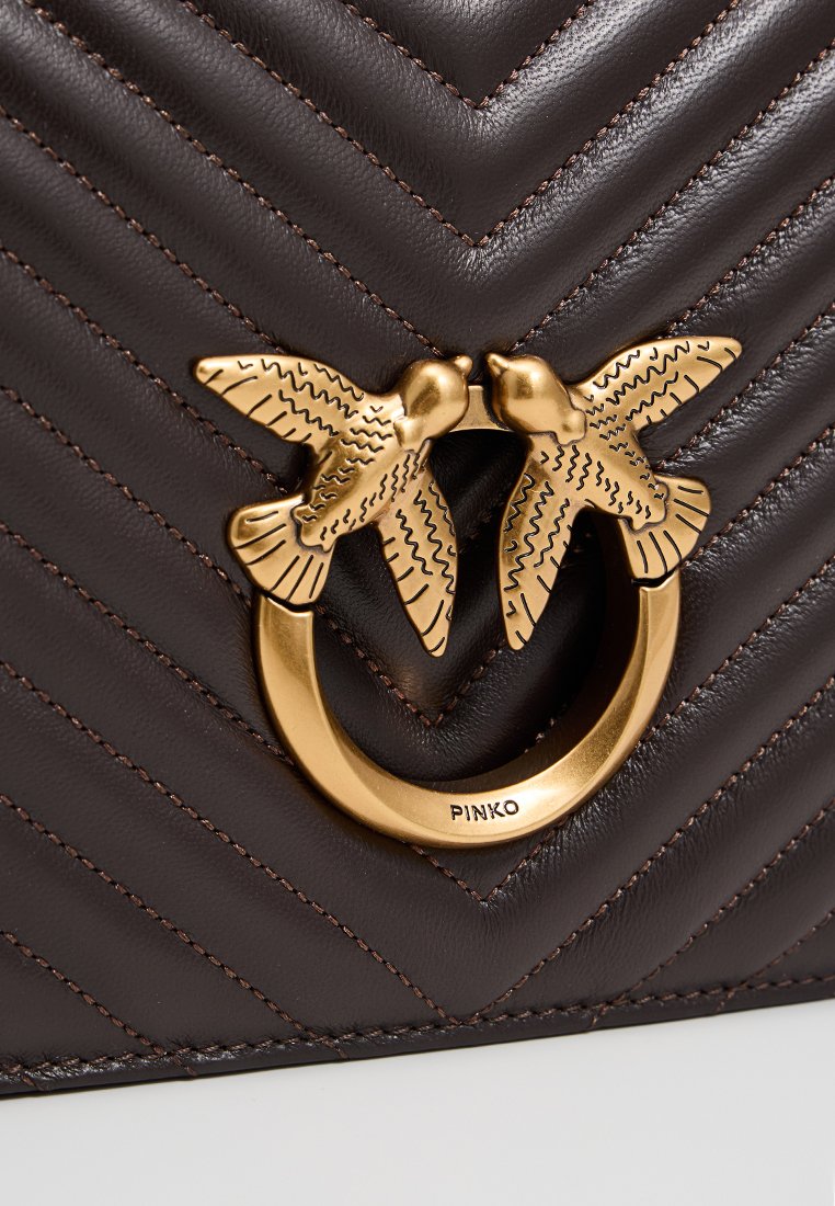 Brązowa skórzana torebka z wzorem w zygzak, z złotym okrągłym elementem ozdobnym w kształcie dwóch całujących się ptaków.