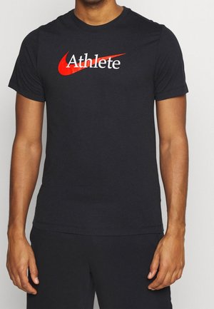 Mand iført en sort t-shirt med en rød Nike swoosh og ordet "Athlete" trykt i hvidt over brystet.