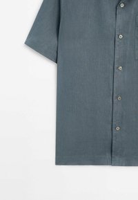 Chemise à manches courtes bleu ardoise avec des boutons et une poche poitrine, présentée à plat sur un fond blanc.