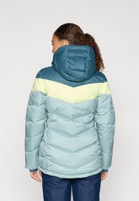 Πουκάμισο με επένδυση σε ανοιχτό μπλε με σκούρο τυρκουάζ επάνω μέρος και κίτρινο-πράσινα διακοσμητικά σε σχήμα βιλάρης. Διαθέτει κουκούλα και υφασμάτινη ραφή.