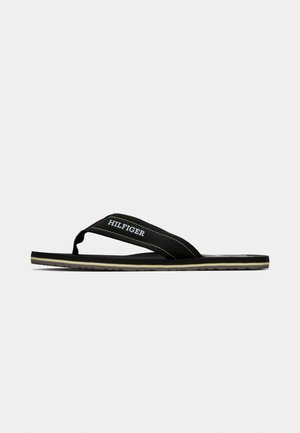Fekete papucs, textúrált fekete gumi talppal, sárga varrással ellátott szövetpánttal és fehér "HILFIGER" logóval.