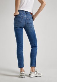 Blå denim skinny jeans med fransad fåll, har två bakfickor och en traditionell dragkedja. Bärs med ljusgrå sneakers.