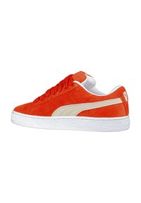 Sneaker in suede arancione con suola in gomma bianca. Le caratteristiche includono lacci tondi, dettagli perforati e una striscia laterale beige con il logo del marchio.