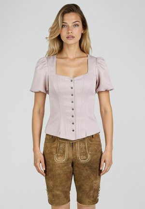 Jeune femme aux cheveux blonds portant un chemisier ajusté rose clair à manches bouffantes et un short en cuir traditionnel marron avec broderies.