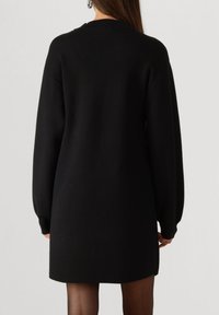 Zwart oversized sweaterjurk met lange mouwen, geribbelde manchetten en een afgeronde halslijn, met een gladde textuur en een zoom tot op de knie.