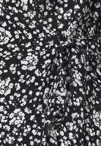 Tissu noir avec petit imprimé floral blanc, montrant un détail de nœud noué au centre.
