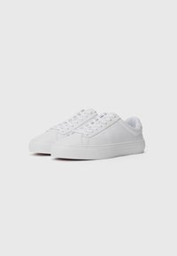 White low-top sneakers with a smooth leather upper and rubber sole, featuring round laces and minimalistic design without visible logos.