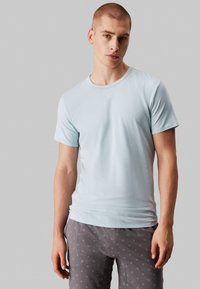 Light blue short-sleeve t-shirt with a round neckline. Soft fabric, smooth texture. Worn with gray patterned pants featuring small white accents.