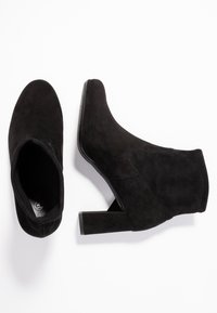 Bottines en suede noir avec un bout pointu et un talon carré épais. Présentent des coutures minimales et une doublure intérieure lisse.