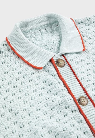 Polo en maille bleu clair à motif texturé, boutons marron et bordure orange le long du col et de la patte de boutonnage.