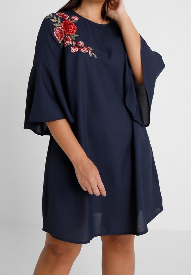 Robe droite bleu marine avec broderie florale sur l'épaule gauche et manches volantées. Fabriquée en tissu léger et texturé.
