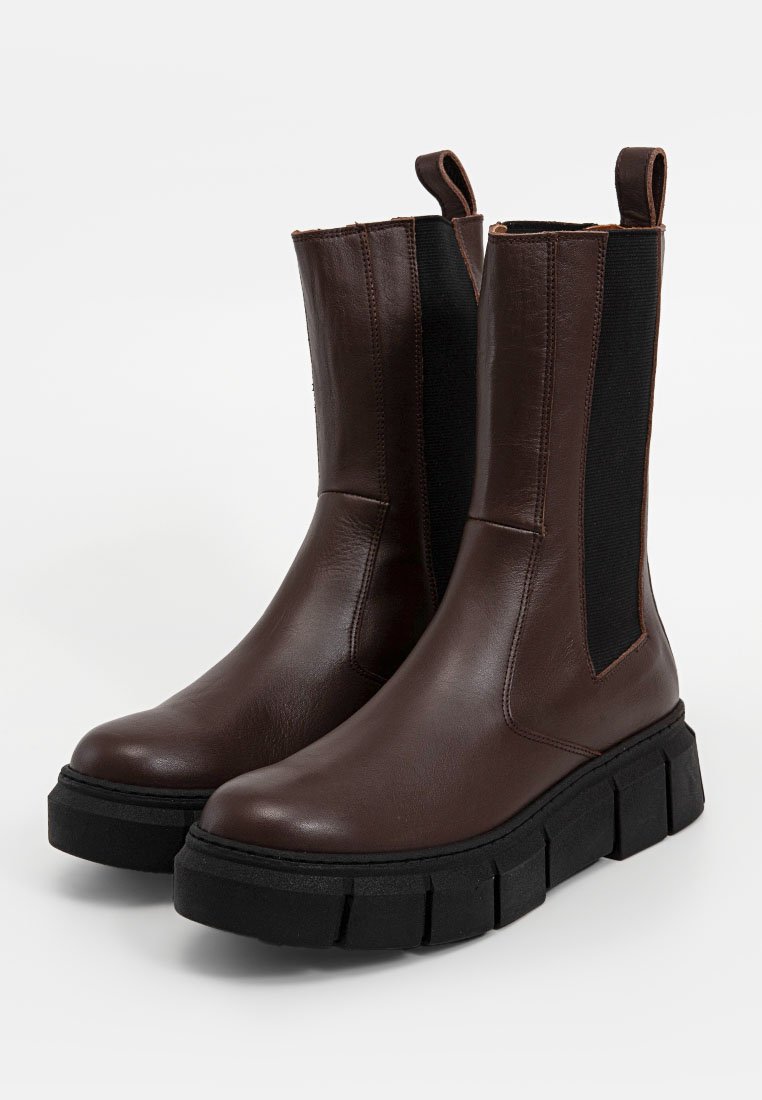 Bottines en cuir marron avec des panneaux élastiques sur les côtés, semelle en caoutchouc noir épaisse et talon rehaussé. Texture lisse et détails minimalistes.