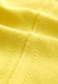 Sárga kötött anyag sima textúrával és kiemelkedő varrási részletekkel, élénk, egyszínű árnyalattal és az egész felületen egységes mintával.
