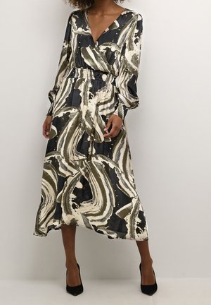 Woman wearing a long-sleeve, V-neck, midi dress with black, white, and olive abstract swirl patterns, paired with black high heels.