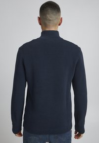 Marineblaues ribbeltes Sweater mit hohem Kragen, strukturiertem Stoff und schmalen Ärmeln, ausgestattet mit einem einfarbigen Rückendesign.