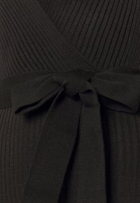 Tissu côtelé noir avec un design croisé, doté d'un détail de taille nouée. La texture est douce et élastique, améliorant l'ajustement du vêtement.