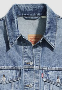 Light blue denim jacket with a classic collar, two chest pockets, silver hardware, and a distinctive brand label stitched inside.