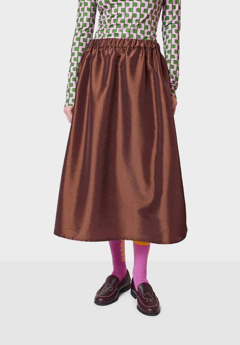 Smeđa, satenska suknja do članaka s nabranim pojasom. Nosila se s jarkim ružičastim čarapama i mokasinkama s razigranim uzorcima.