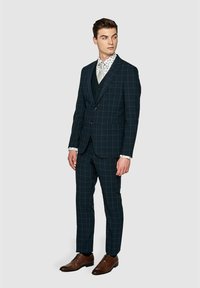 Granatowy garnitur w kratkę o dopasowanym kroju i klapie typu notch, zestawiony z białą koszulą w wzory i brązowymi skórzanymi butami.