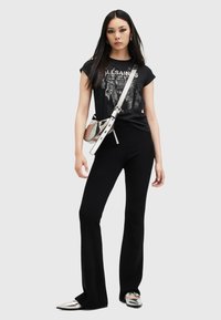 Camiseta gráfica negra, pantalones negros acampanados y zapatos planos metálicos plateados. Incluye un bolso cruzado plateado y cabello lacio y largo.