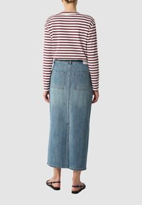 Camicia a maniche lunghe a righe con linee rosse e bianche; gonna di jeans blu a vita alta; due tasche posteriori; sandali neri; silhouette dritta.