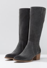 Para ciemnoszarych zamszowych botków do połowy łydki z drewnianymi obcasami i zamkami bocznymi na białej powierzchni i jasnoszarym tle.