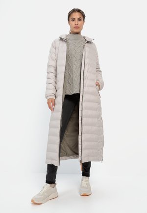 Gevoerde lange jas in lichtbeige met een capuchon, geribbelde textuur, ritssluiting aan de voorkant en zakken, gecombineerd met een grijs gebreid vest en zwarte jeans.