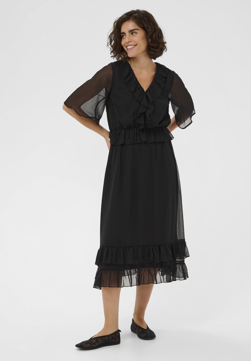 Robe noire avec un décolleté en V, manches courtes à volants et volants superposés à la taille et à l'ourlet. Tissu transparent et léger avec une silhouette fluide.