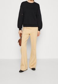 Felpa nera con maniche a palloncino caratterizzata da forature a occhio, abbinata a pantaloni a gamba larga crema e calzature nere. Accessorio a borsa marrone.