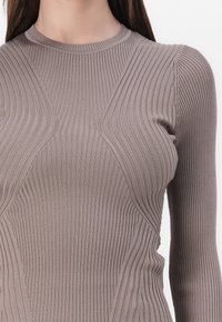 Braun geripptes Langarmoberteil mit hohem Kragen und kantigen Designelementen. Der Stoff hat eine glatte Textur mit Stretch.