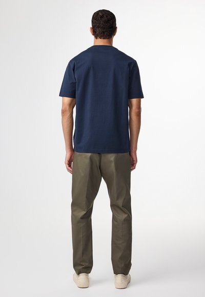 Marineblaue Baumwoll-T-Shirt mit Rundhalsausschnitt und kurzen Ärmeln, kombiniert mit olivgrünen Hosen und hellen Schuhen. Minimales Design.