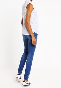 Ärmlös randig skjorta i ljusblått och vitt, tillsammans med mörkblå tajta jeans och svarta och vita sneakers. Avslappnad outfit från en sidovy.