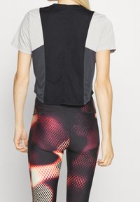 Top de manga corta con bloques de color negro y gris, acompañado de leggins texturizados con un patrón de malla y acentos vibrantes en rojo y naranja.