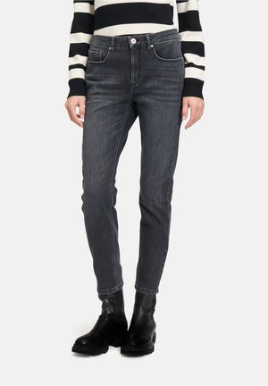 Schwarz-graue hochgeschnittene Jeans mit schlankem Schnitt, Fünf-Taschen-Design, feinen Nähten und getragenem Look, kombiniert mit schwarzen Knöchelstiefeln.