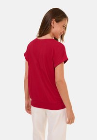 Haut rouge à manches courtes avec un col rond et une coupe décontractée. Présente une texture unie et un ourlet légèrement froncé.