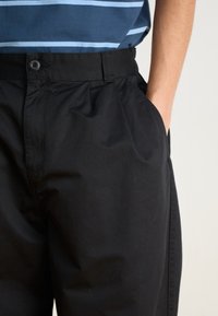Pantalons en coton noir à coupe décontractée, avec fermeture à bouton et poches latérales. Texture lisse, sans motifs visibles.