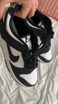 Fekete-fehér Nike sportcipők, sima bőr felsőrésszel, perforált orral és hagyományos fűzőrendszerrel. Az talp texturált mintázatú.