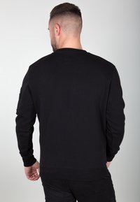 Sweatshirt noir avec un col rond, des poignets et une taille côtelés. Présente une poche zippée sur la manche gauche. Texture lisse et douce.
