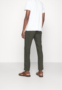 Pantaloni slim-fit verde oliva realizzati in un tessuto leggero, abbinati a sandali marroni. La t-shirt bianca presenta una vestibilità rilassata e un colletto a girocollo.