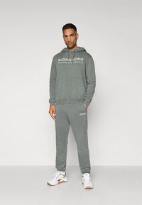 Gray fleece hoodie with front pocket and white text, paired with matching joggers featuring logo detail. Worn with white athletic shoes.