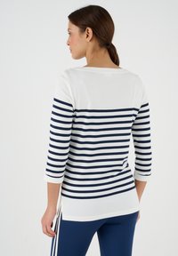 Gestreifter Pullover, weiß mit navyblauen horizontalen Streifen, verfügt über Drei-Viertel-Ärmel, Seitenschlitze und einen Bootsausschnitt mit Knopfdetails.