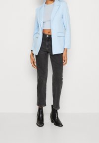 Blazer bleu clair sur mesure, crop top gris, jean noir taille haute, et bottines noires à finition texturée avec talons carrés.