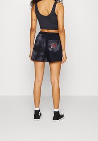 Černé šortky s batikováním a zadní kapsou zdobenou červeným vyšívaným motivem, doplněné o černý tílko bez rukávů a černé vysoké tenisky.