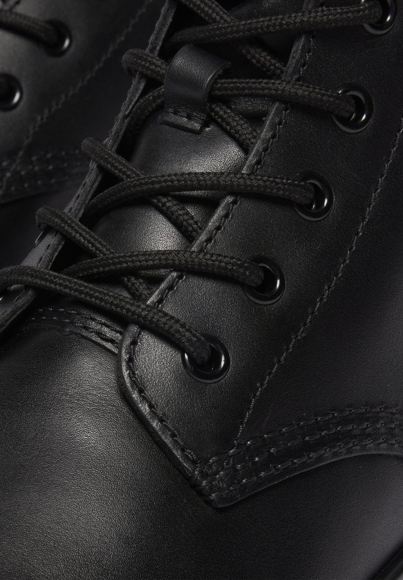 Gros plan sur une botte en cuir noir avec des lacets ronds noirs passés à travers des œillets en métal et des coutures détaillées.