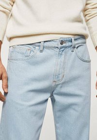 Jeans de denim azul claro con corte recto, que cuentan con bolsillos delanteros, cierre con cremallera y costuras en contraste. La tela parece suave y lisa.