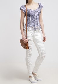 Haut à manches courtes à carreaux avec bord en dentelle, associé à un jean blanc déchiré et des baskets décontractées. Sac bandoulière marron inclus.