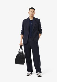 Marinblazer och byxor i texturerad tyg, matched med en marinblå polo, svart väska och vita sneakers med svarta accenter.