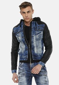Denim jacket with black leather sleeves, faded blue front, multiple pockets, and button detailing, paired with a black hoodie underneath.