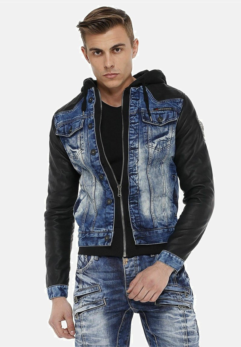 Denim jacket with black leather sleeves, faded blue front, multiple pockets, and button detailing, paired with a black hoodie underneath.